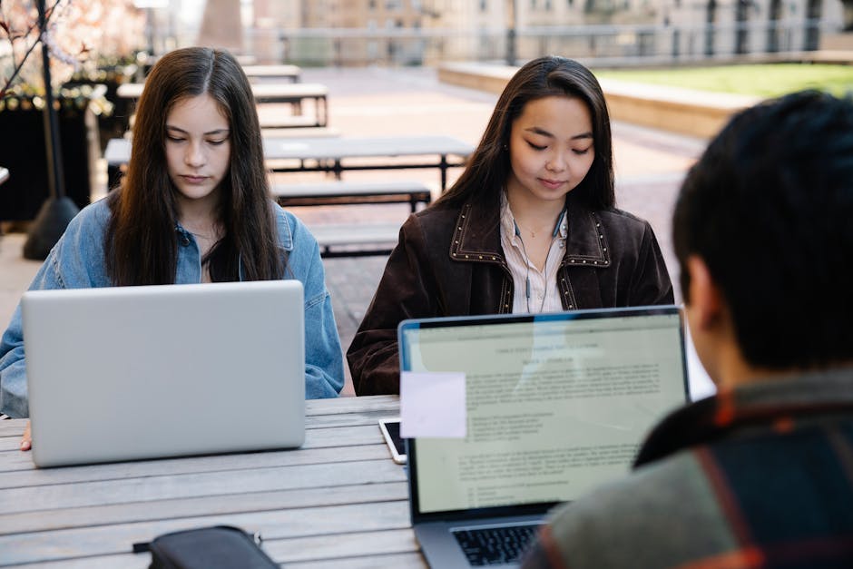 Two students focus on studying with laptops at an outdoor university setting